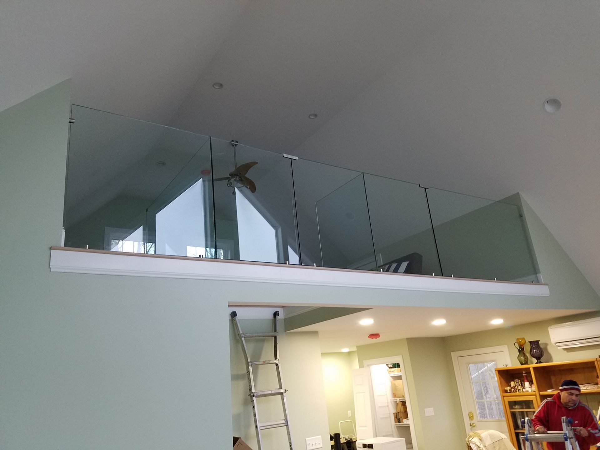 A man is standing on a ladder in a living room next to a glass railing.