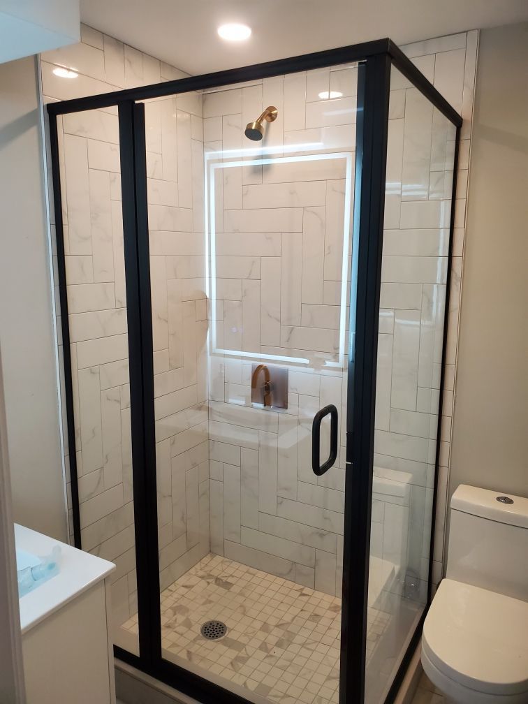 A bathroom with a shower , toilet , sink and mirror.