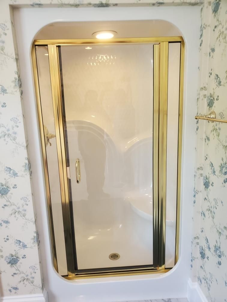 A white shower stall with a gold trim in a bathroom