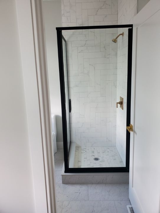 A bathroom with a walk in shower with a black frame