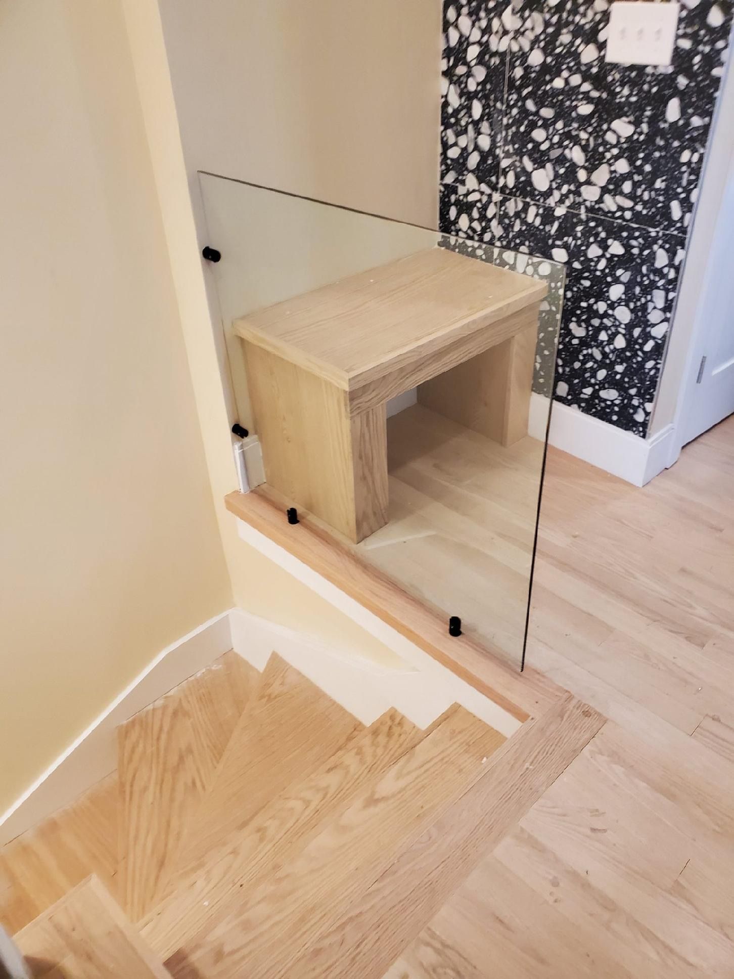 A wooden staircase with a glass railing and a wooden stool.