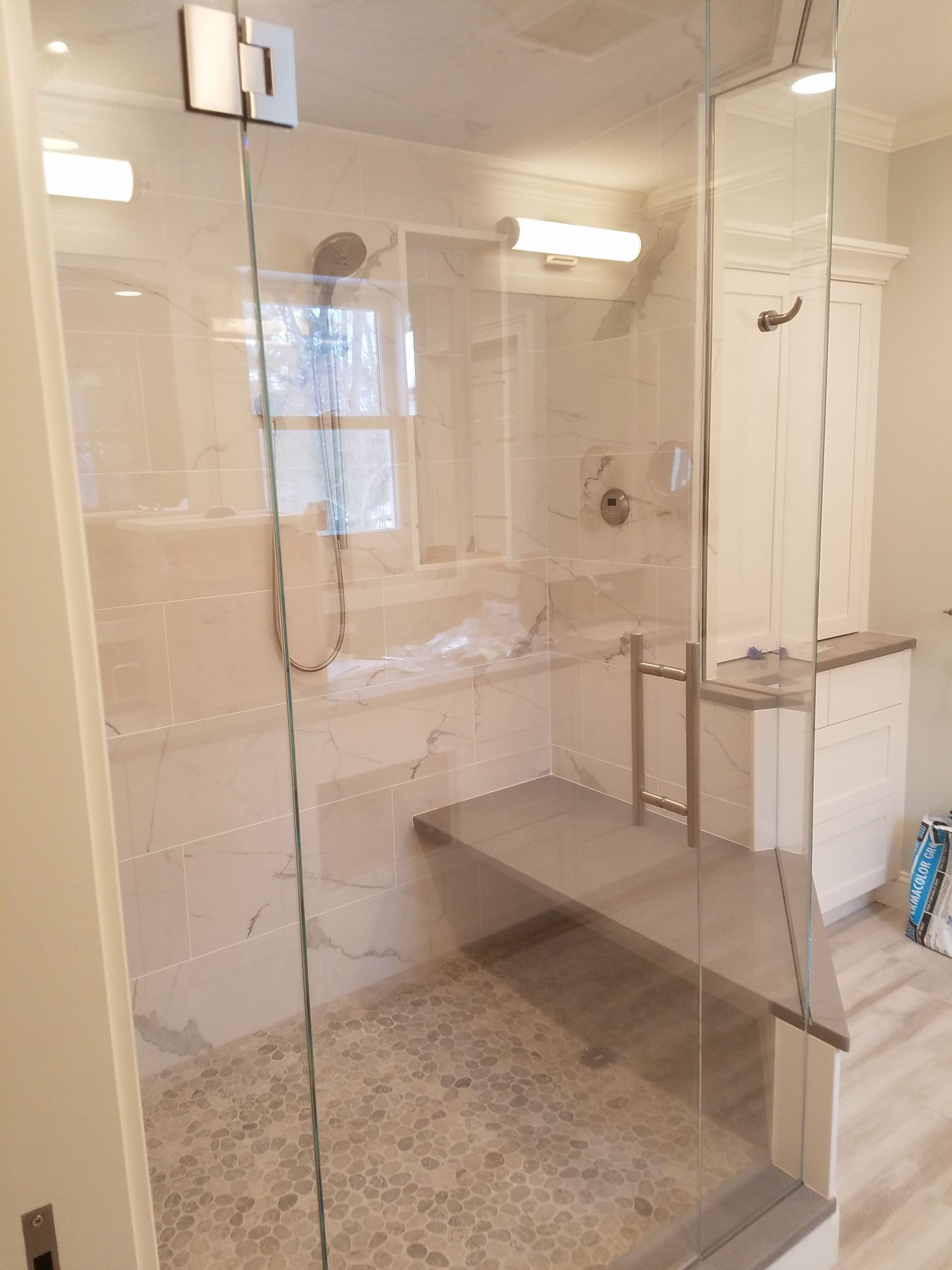 A bathroom with a glass shower door and a bench.