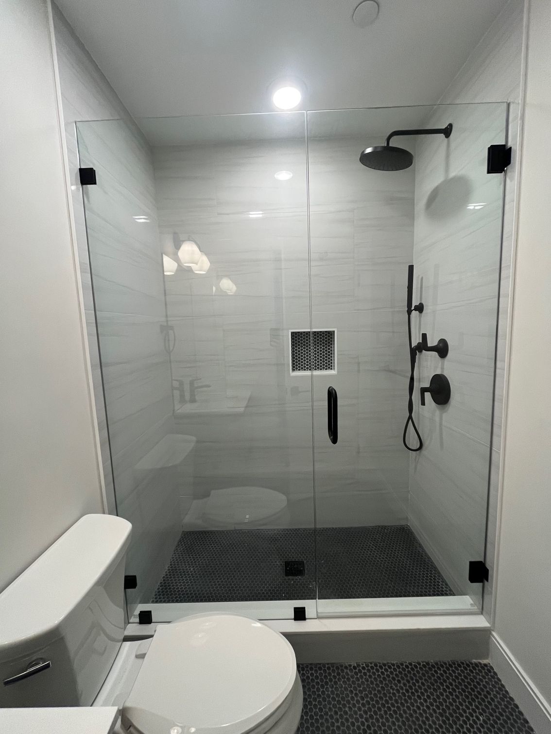 A bathroom with a toilet , sink and shower with a glass door.