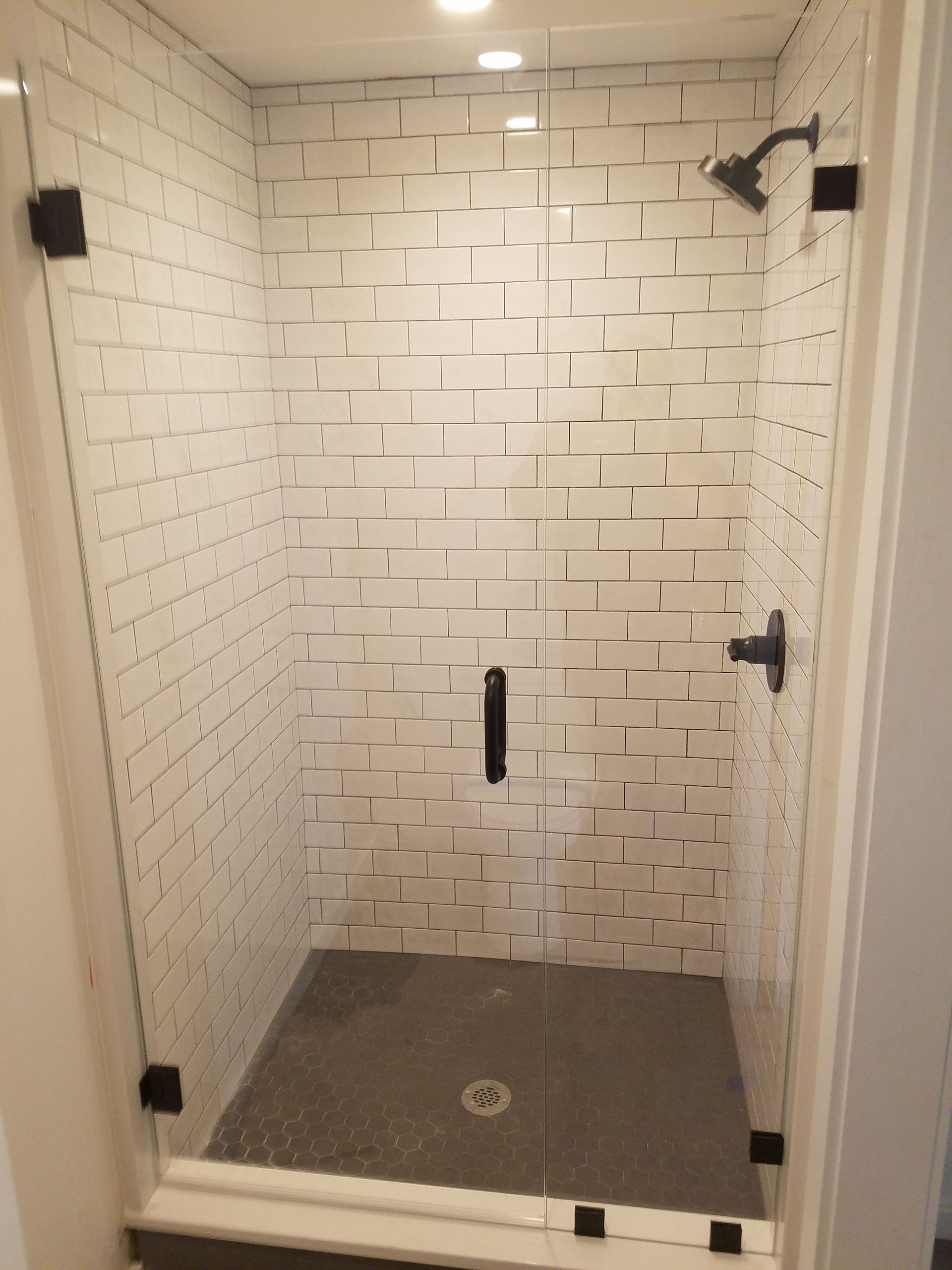 A shower with white tiles and a black shower head