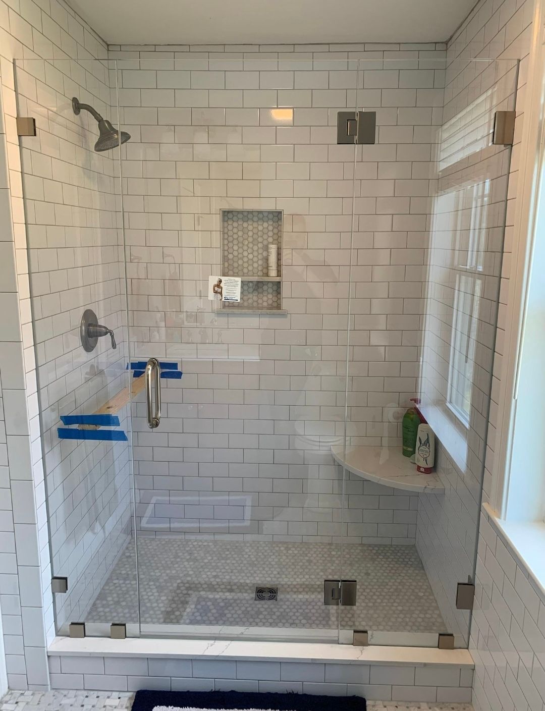 A bathroom with white brick walls and a walk in shower with a glass door.