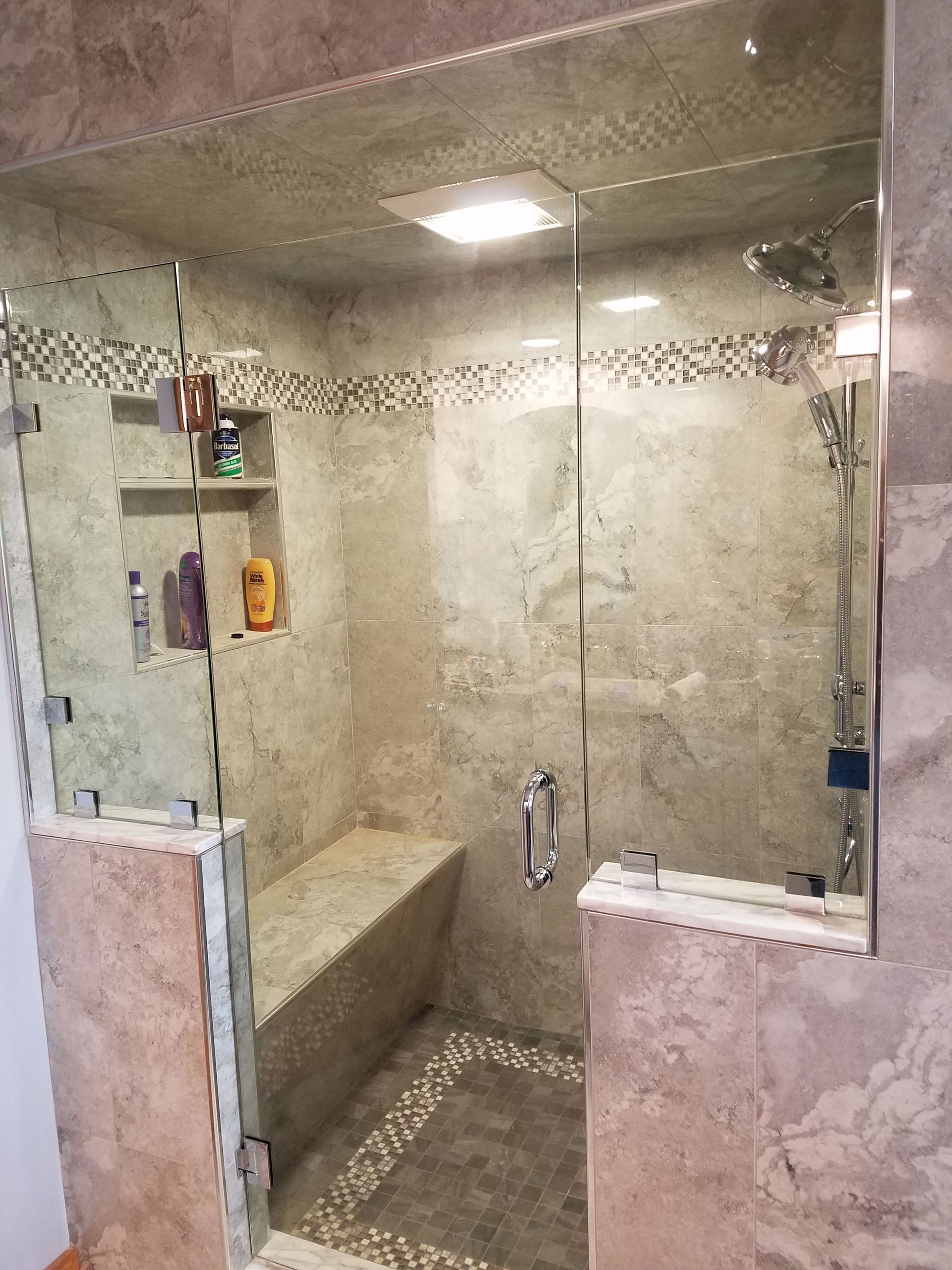 A bathroom with a walk in shower with a glass door and a bench.