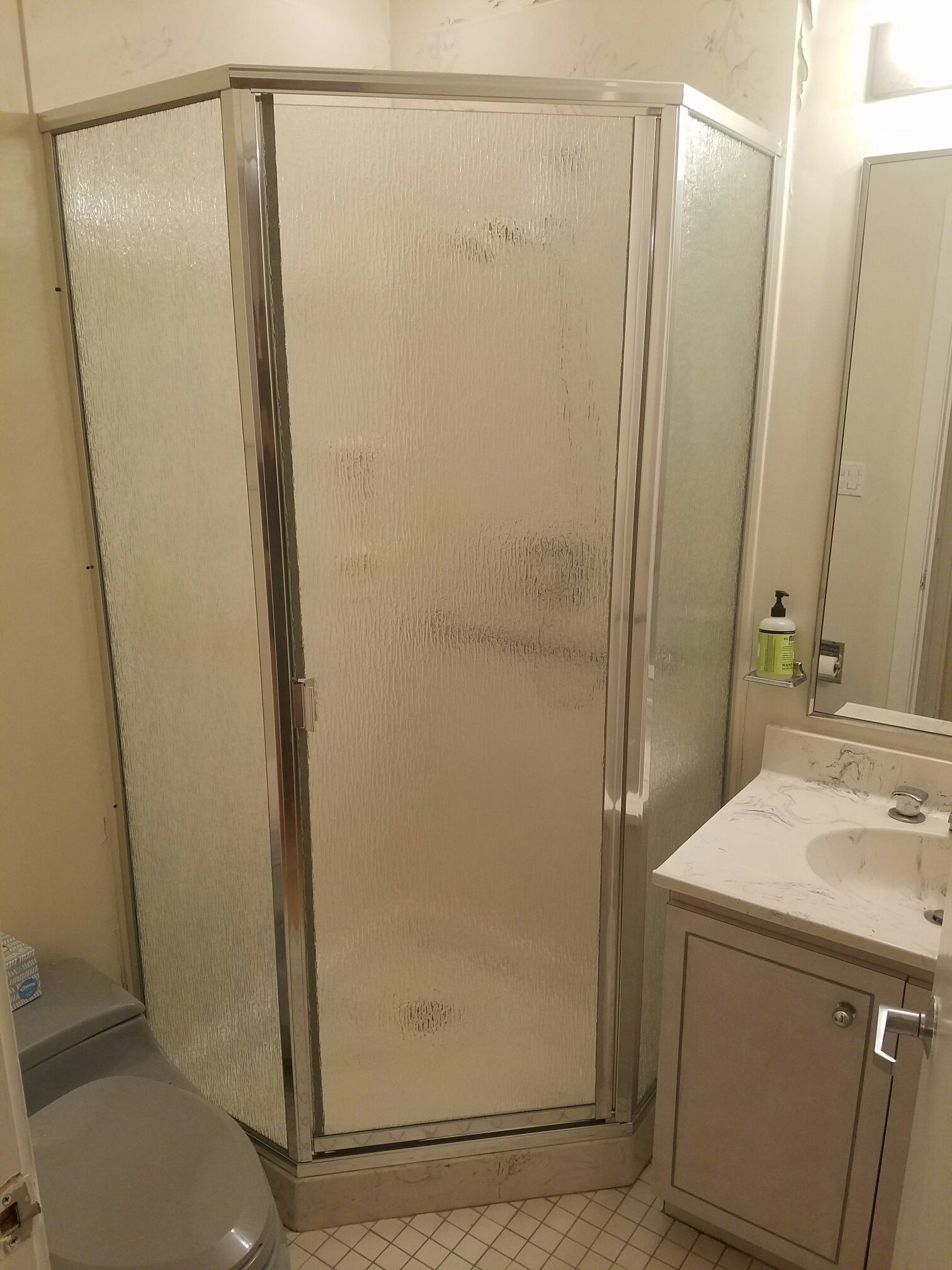 A bathroom with a shower , toilet , sink and mirror.