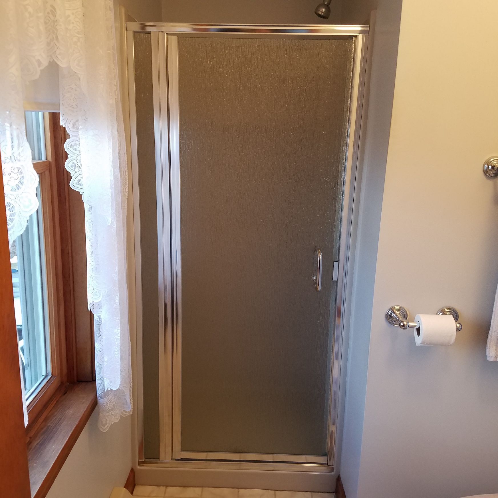 A bathroom with a shower door and a toilet paper holder