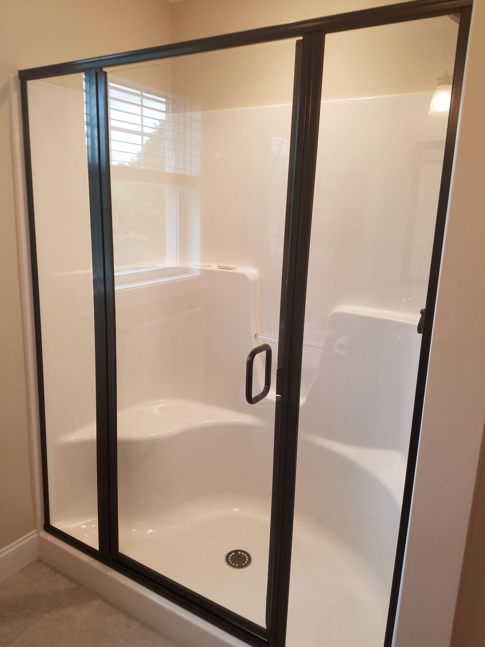 A shower stall with a black frame and sliding glass doors in a bathroom.
