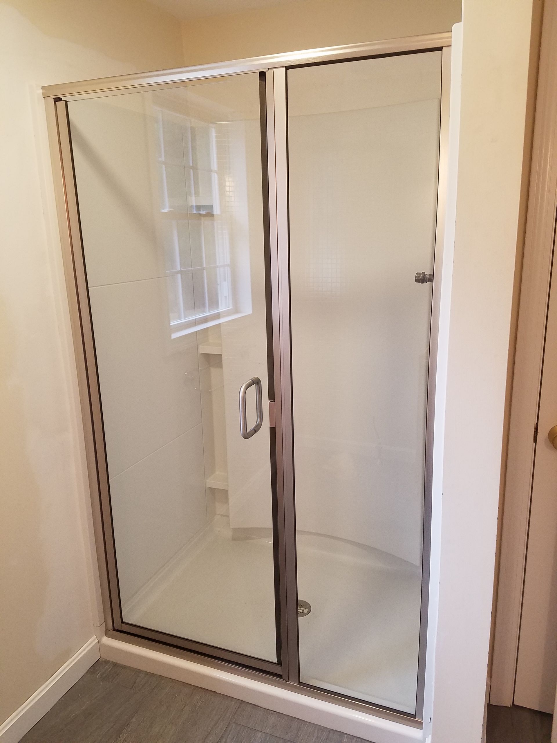 A bathroom with a glass shower door and a window.