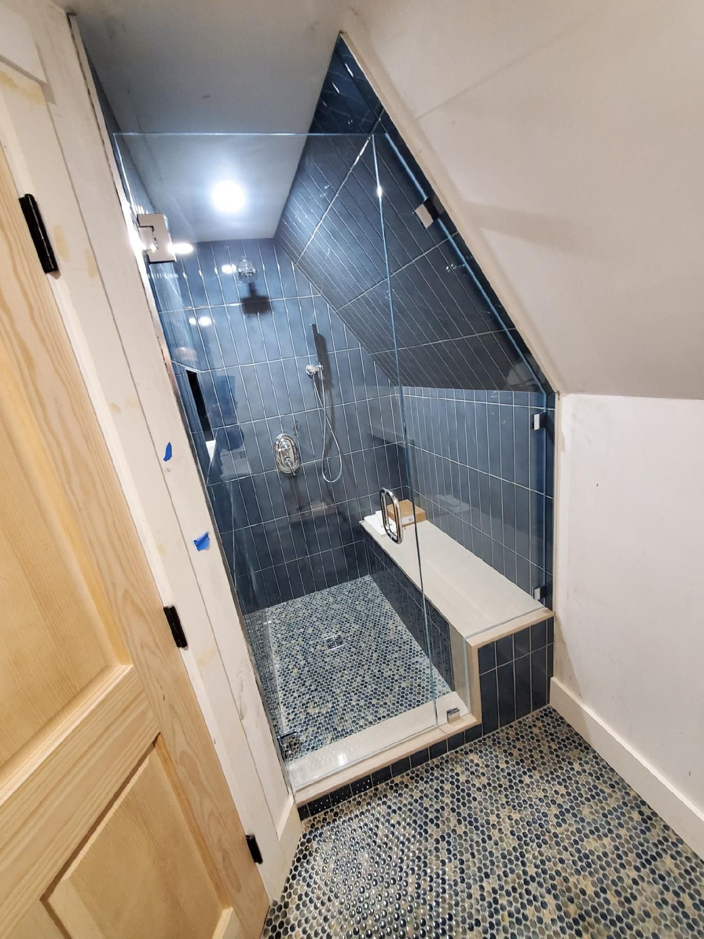 A bathroom with a shower with a glass door and a bench.