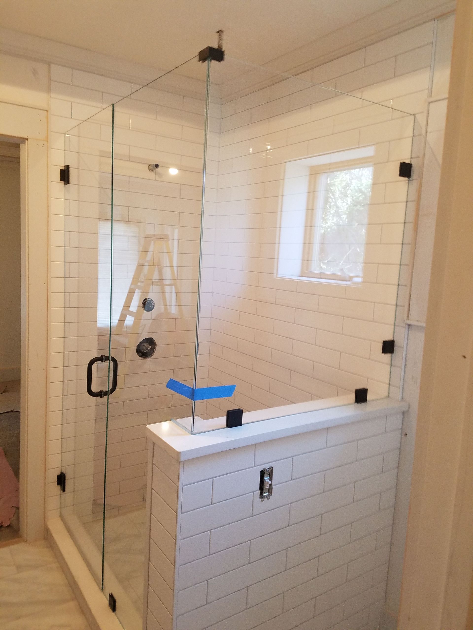 A bathroom with white tiles and a glass shower door.