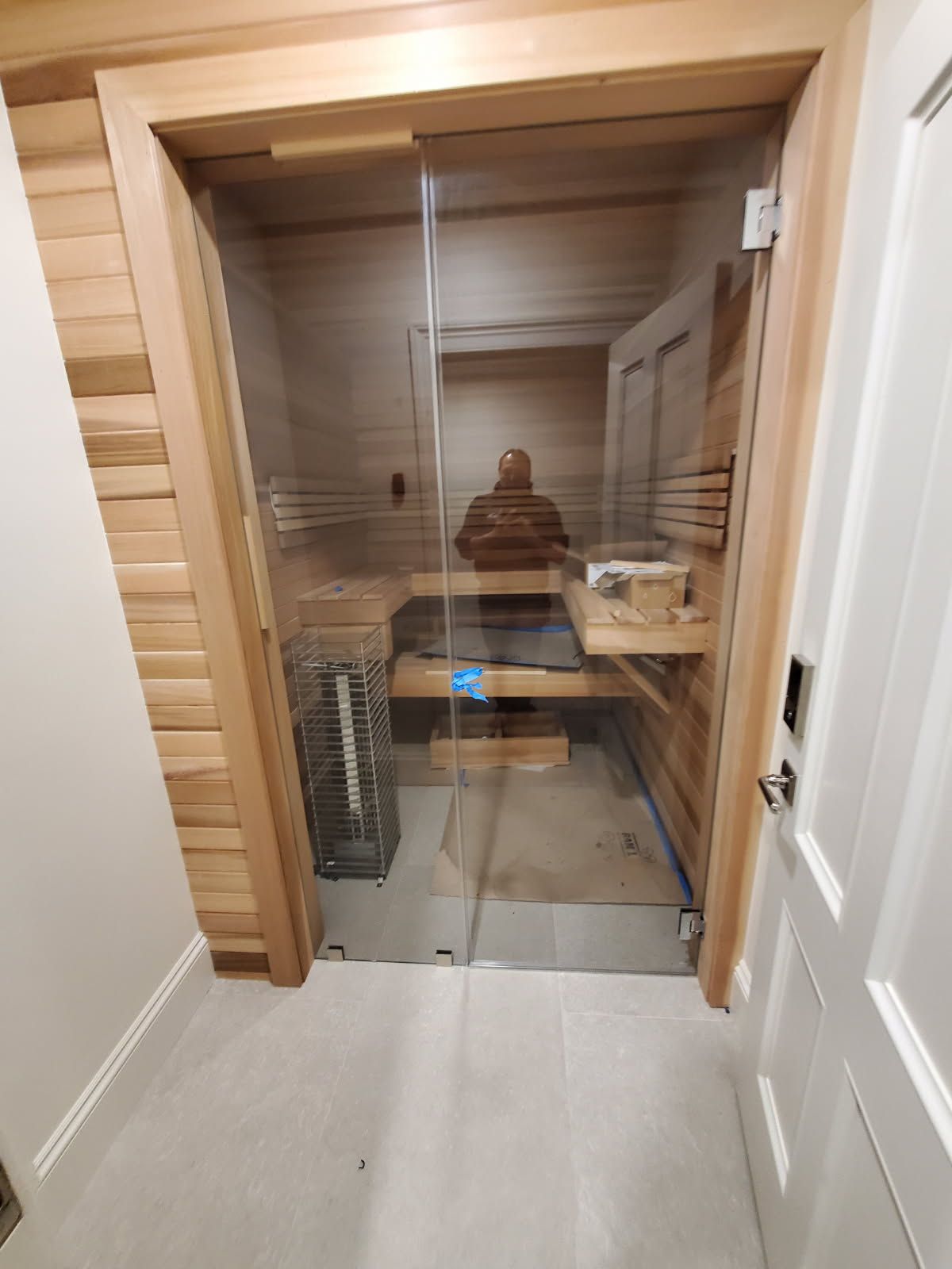 A man is sitting in a sauna with a glass door.