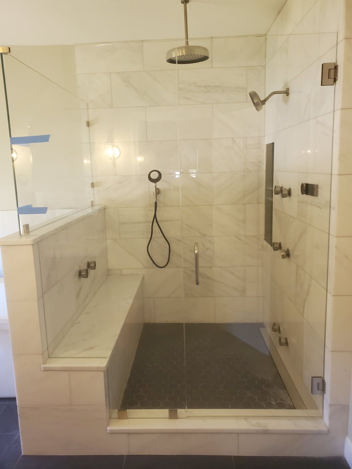 A bathroom with a walk in shower with a bench and a shower head.