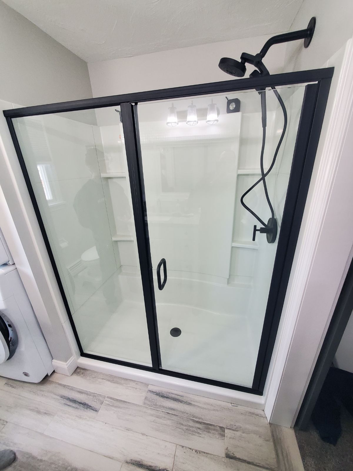 A bathroom with a black shower door and a shower head.
