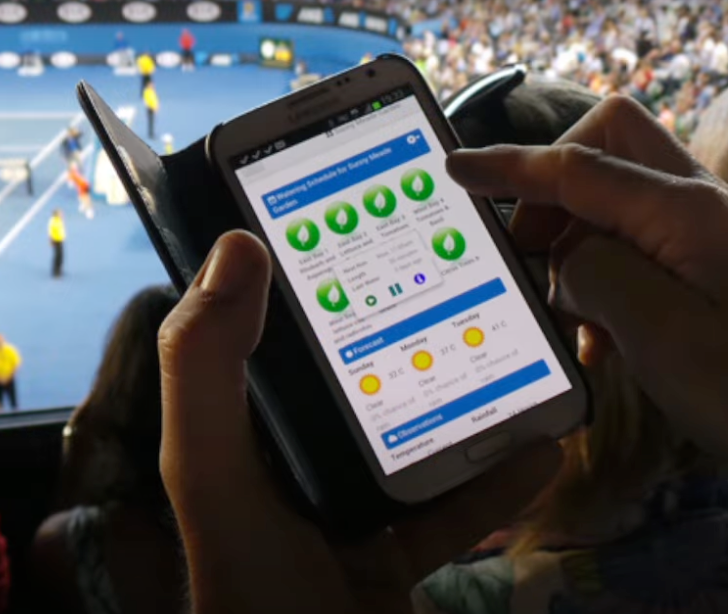 A person is holding a cell phone in front of a tennis court