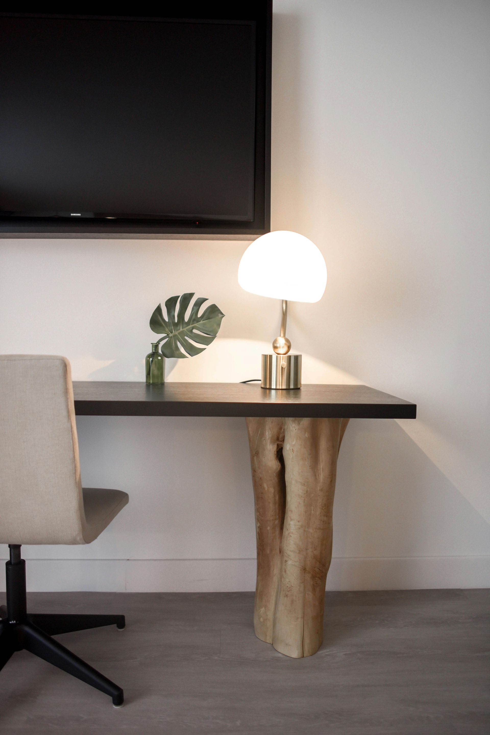 Desk with live-edge leg, lamp, and TV on white wall, beside an office chair.