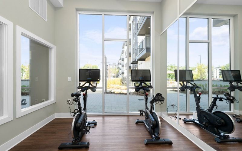 Interior fitness room with three stationary bikes facing large windows.