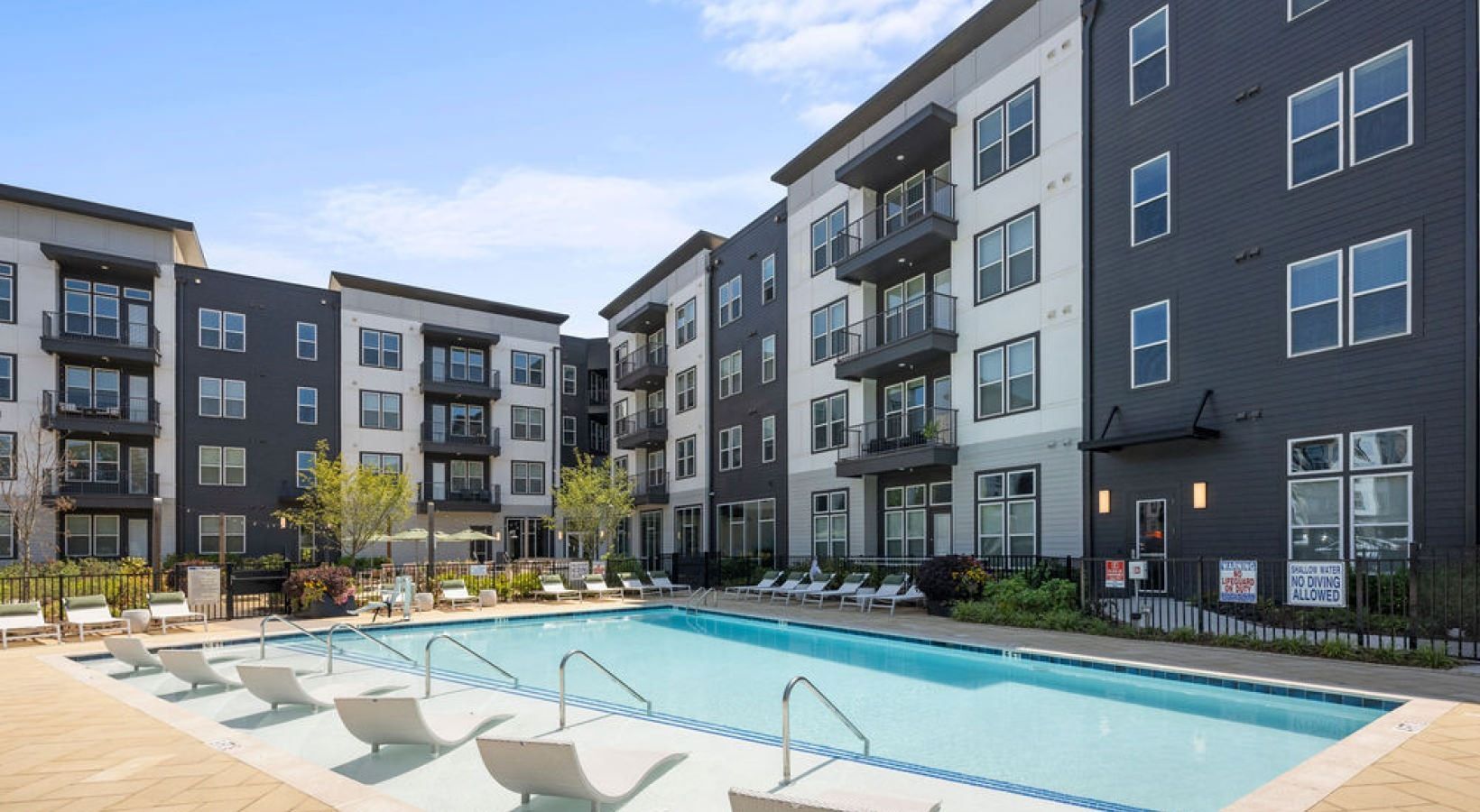 Outdoor pool at an apartment complex with lounge chairs and surrounding buildings.
