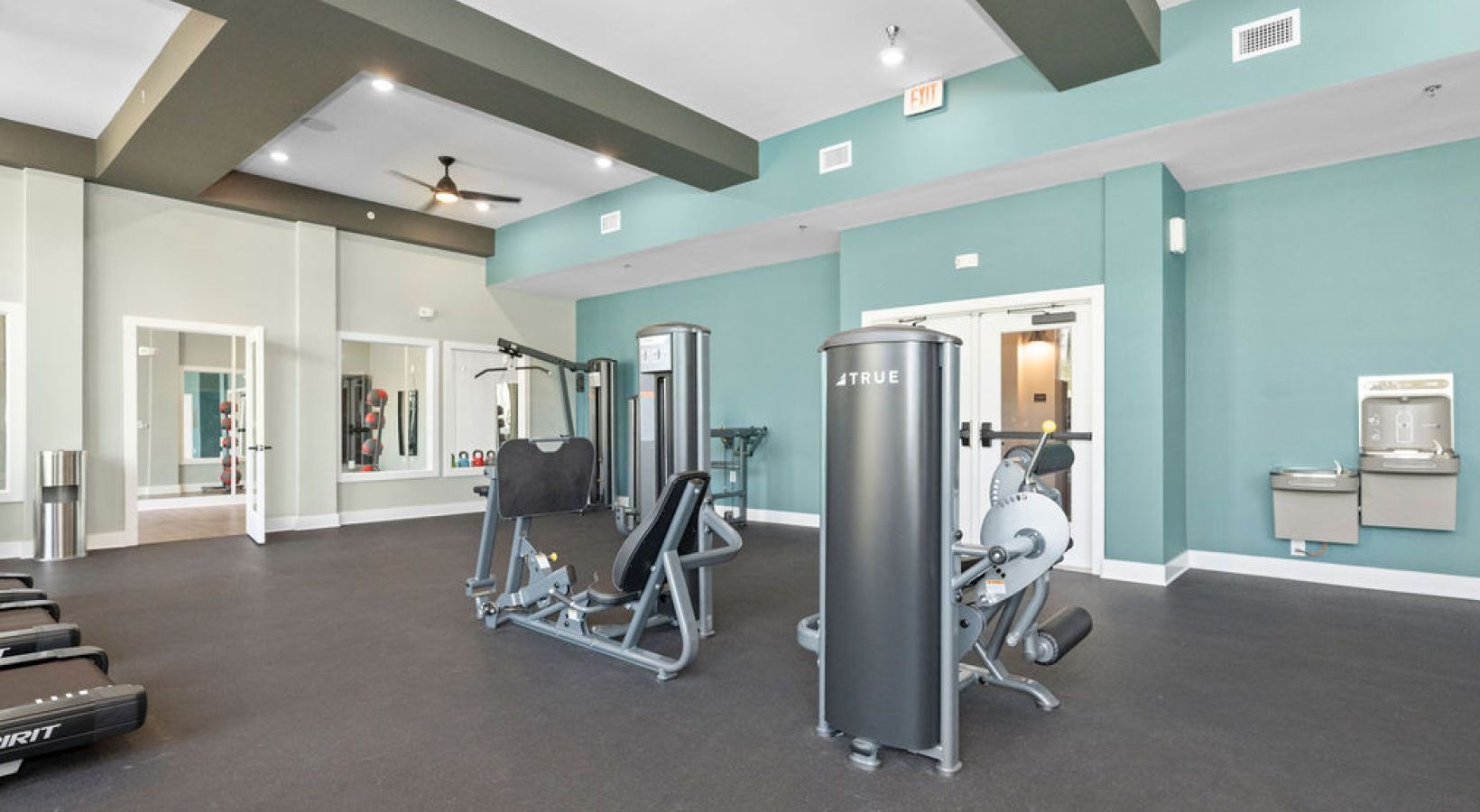Well-lit community gym with cardio machines, weight equipment, and mirrors.