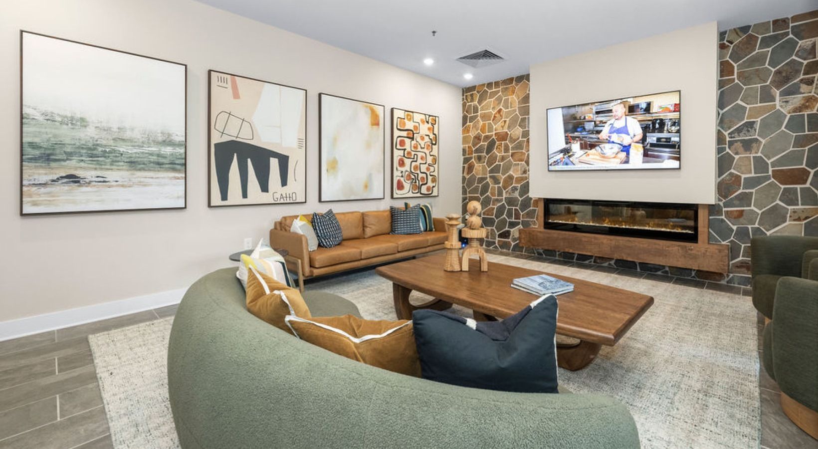 Lounge area with curved green sofa, wall art, stone fireplace wall, and mounted TV.