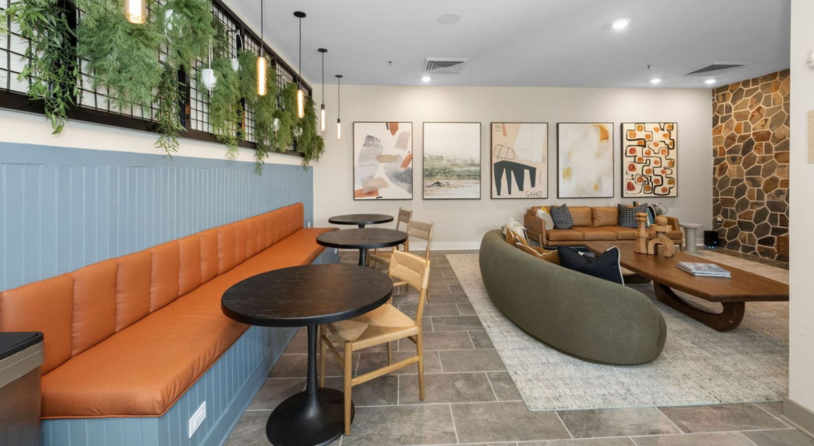 Interior community lounge with orange bench seating, round tables, and modern seating area.