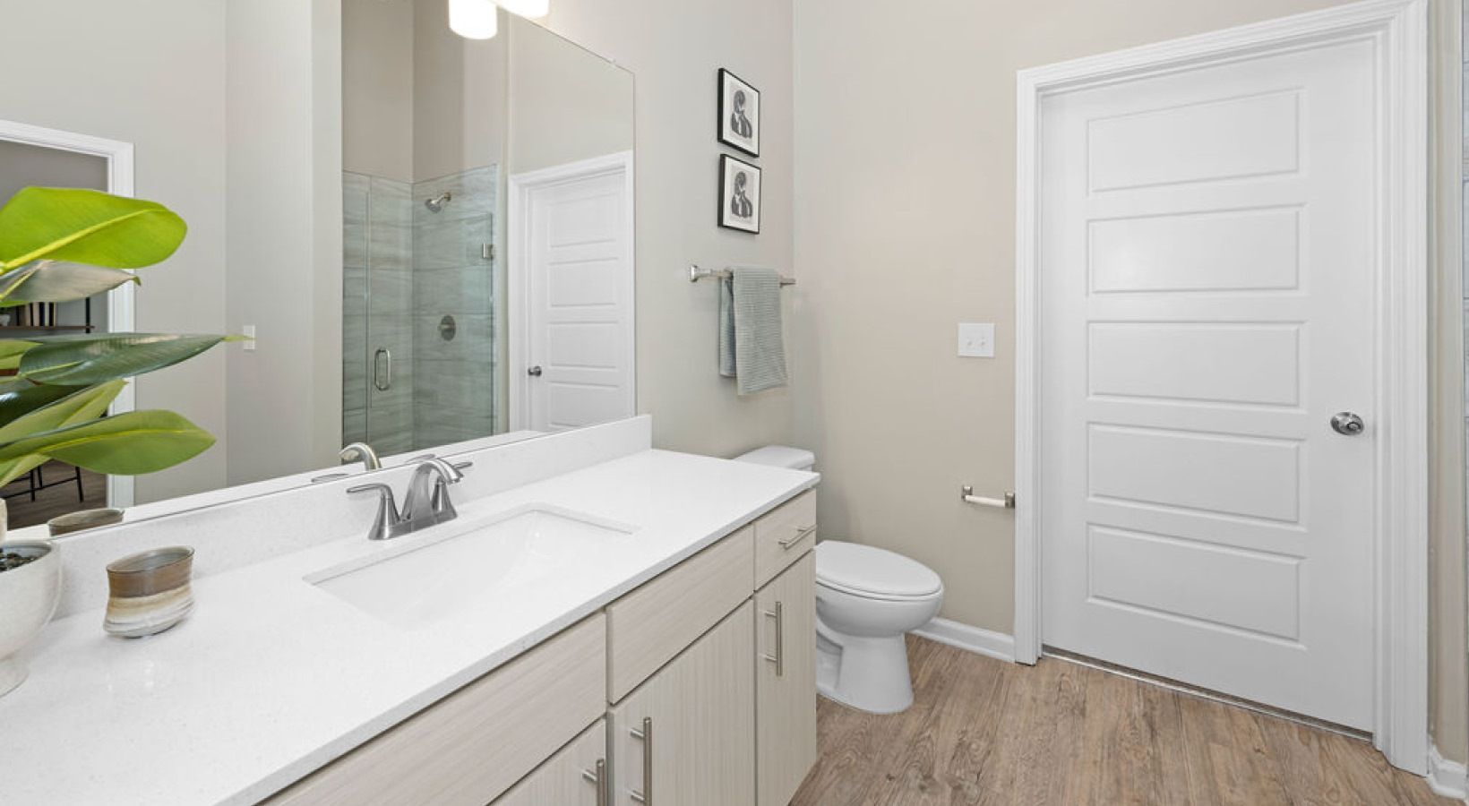 Modern apartment bathroom with a white countertop, single sink, glass shower, toilet, and towel bar.