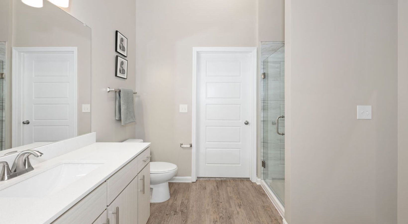 Modern bathroom in an apartment with a white vanity, sink, toilet, and glass shower enclosure.