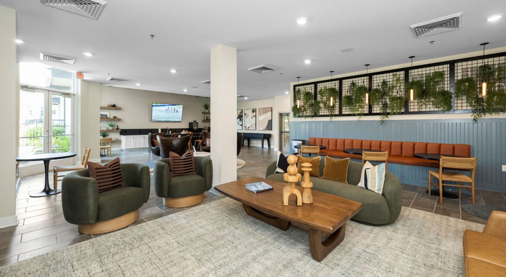 Indoor community lounge with green curved chairs, a wooden coffee table, and a wall-mounted TV.