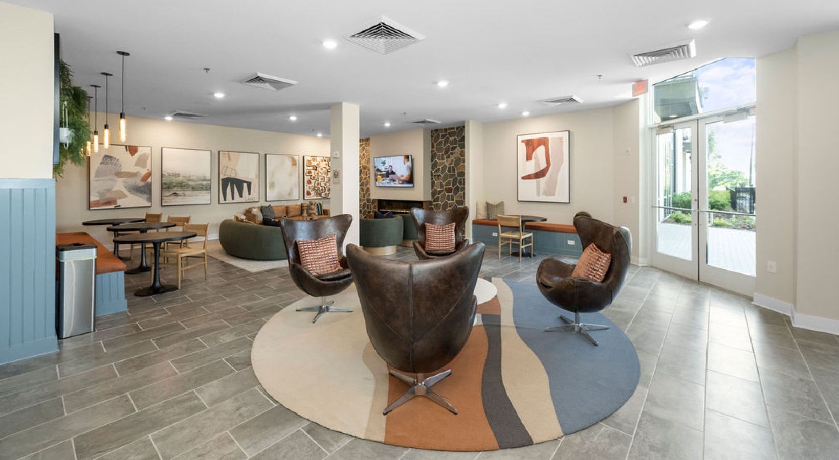 Bright community lounge with leather chairs, wall art, and large glass doors.