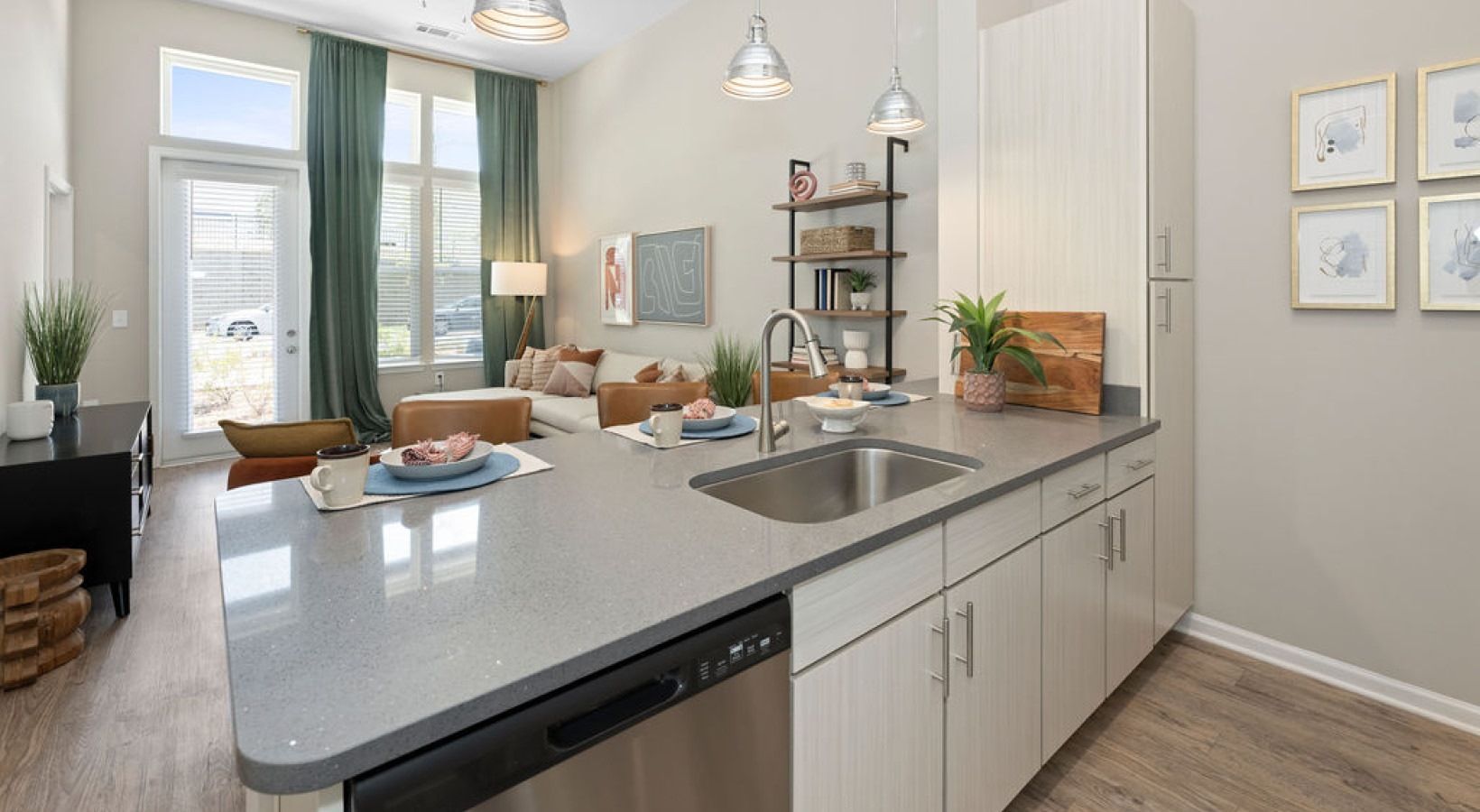 Open-concept kitchen with a gray quartz island, stainless steel sink and dishwasher, and a living area in the background.