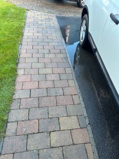 A white car is parked on a sidewalk next to a puddle of water
