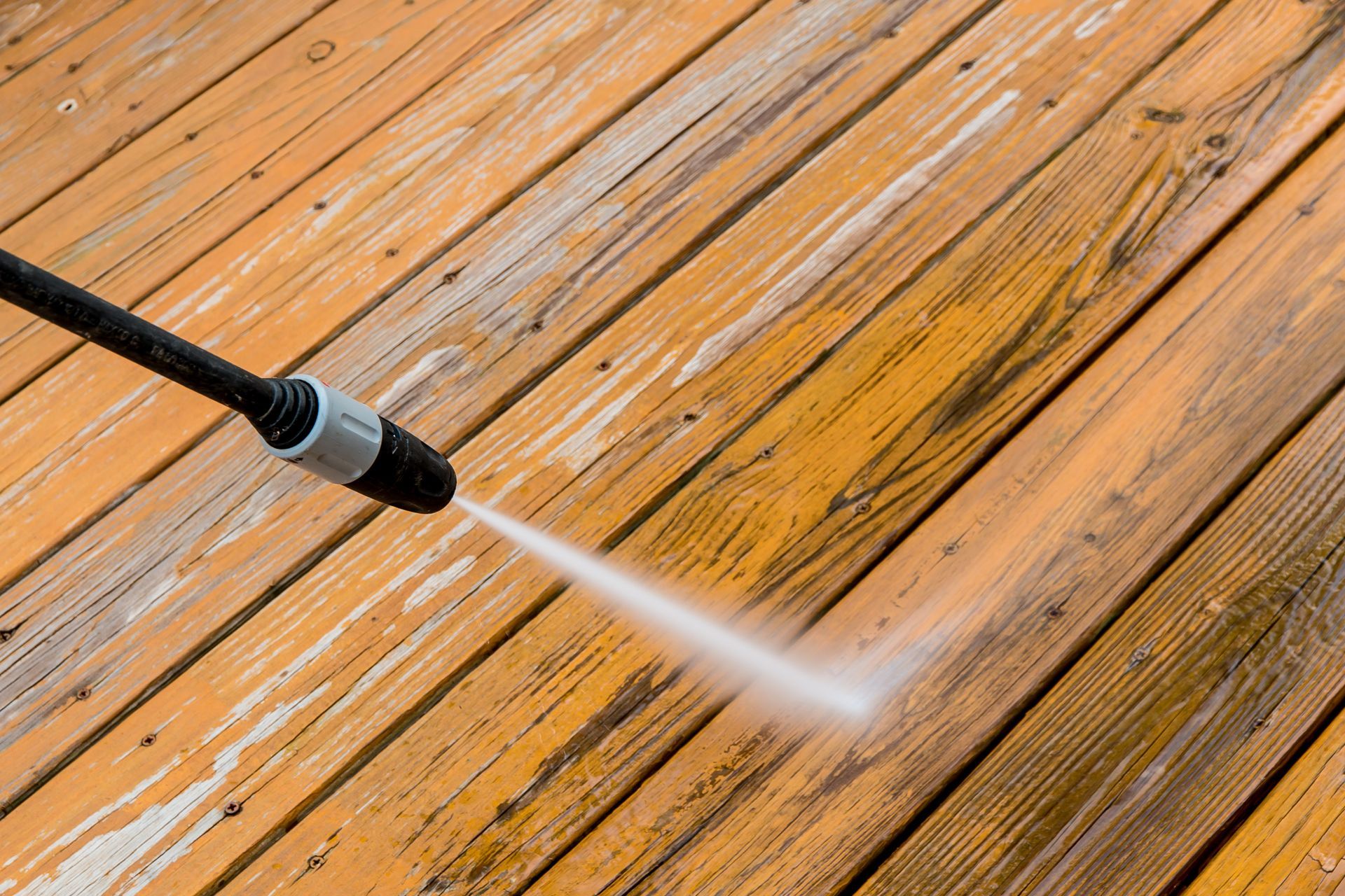 a person is using a high pressure washer to clean a wooden deck .
