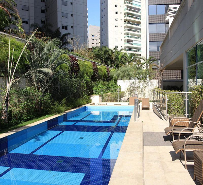 Piscina ao ar livre do eConfor Vila Olímpia, com área de lazer elegante cercada por vegetação e vista urbana de alto padrão.