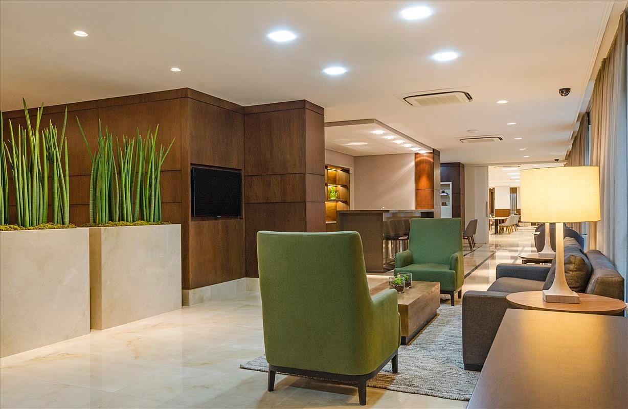 Uma sala de estar com cadeiras verdes, um sofá, uma mesa e um abajur.