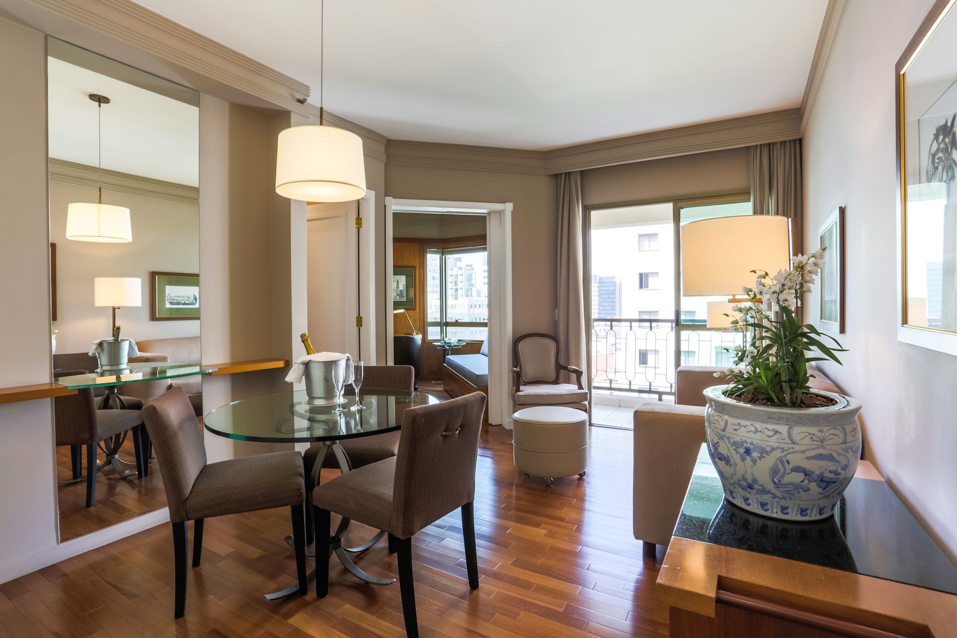 Um estúdio luminoso e moderno com sofá cinza, uma pequena mesa de jantar, uma kitchenette e uma varanda com vista.