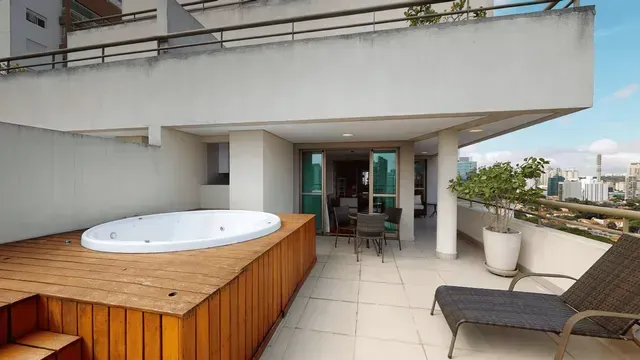 Uma banheira de hidromassagem branca em um deck de madeira ao lado de uma espreguiçadeira em uma varanda com vista para o horizonte da cidade.