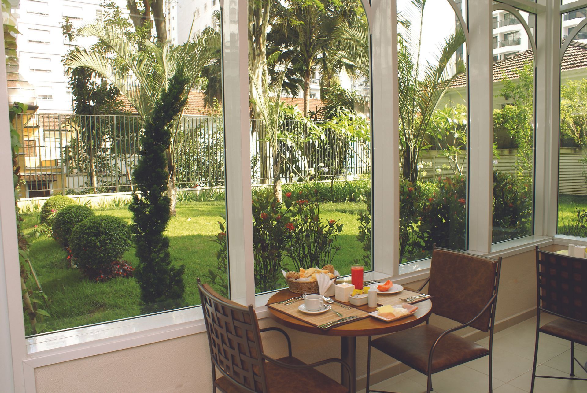 Café da manhã no eConfor Jardins, servido em área envidraçada com vista para jardim verde e paisagismo bem cuidado.