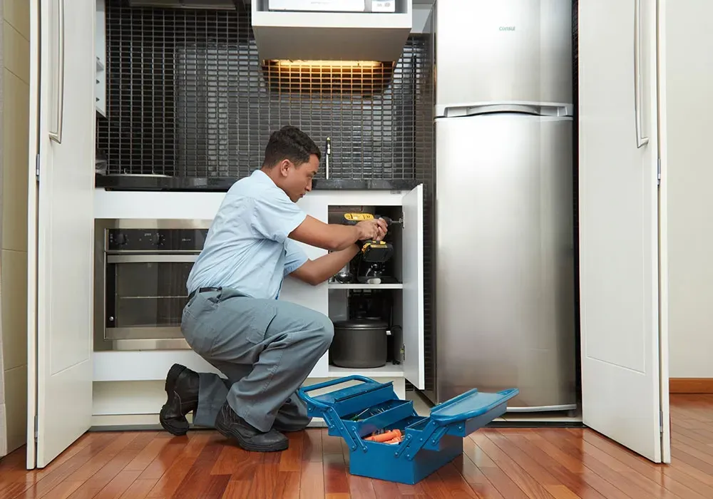 Um homem está trabalhando em uma geladeira na cozinha.