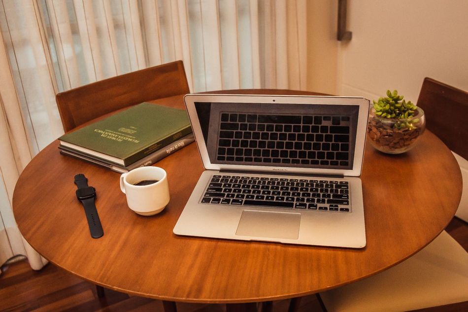 Um laptop está sobre uma mesa de madeira ao lado de uma xícara de café.