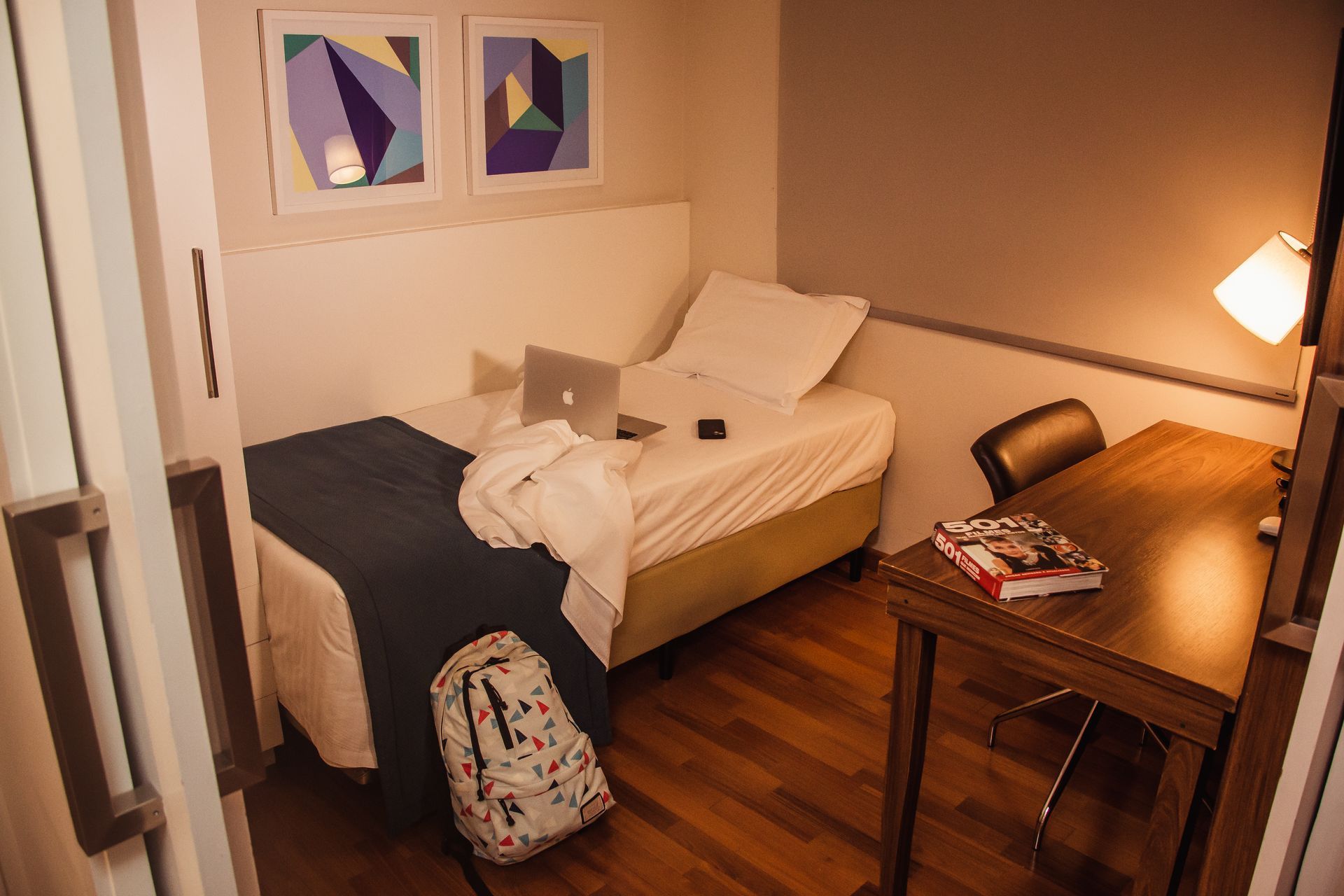 Um quarto com uma cama de solteiro, escrivaninha e laptop.