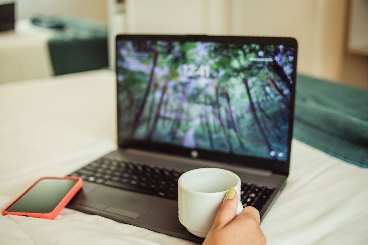 Uma pessoa está segurando uma xícara de café em frente a um laptop.