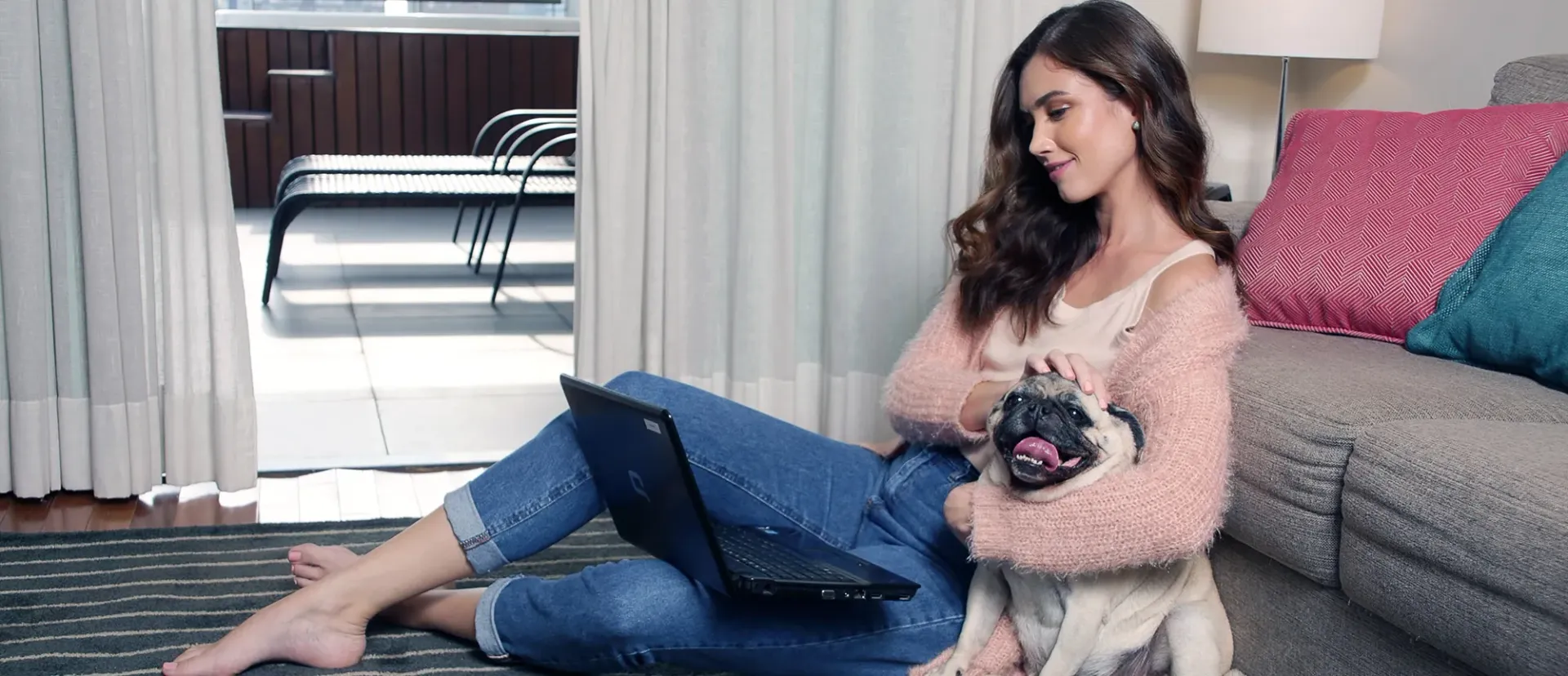 Uma mulher está sentada no chão segurando um cachorro e usando um laptop.