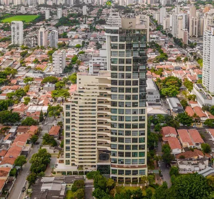 Vista aérea de um edifício residencial moderno e alto, com fachada em camadas, situado em um bairro residencial denso.