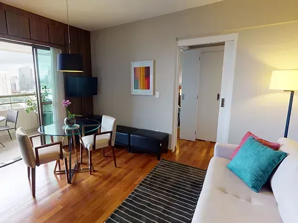 Uma sala de estar moderna com área de jantar, um sofá com almofadas coloridas, piso de madeira e uma mesa com tampo de vidro.