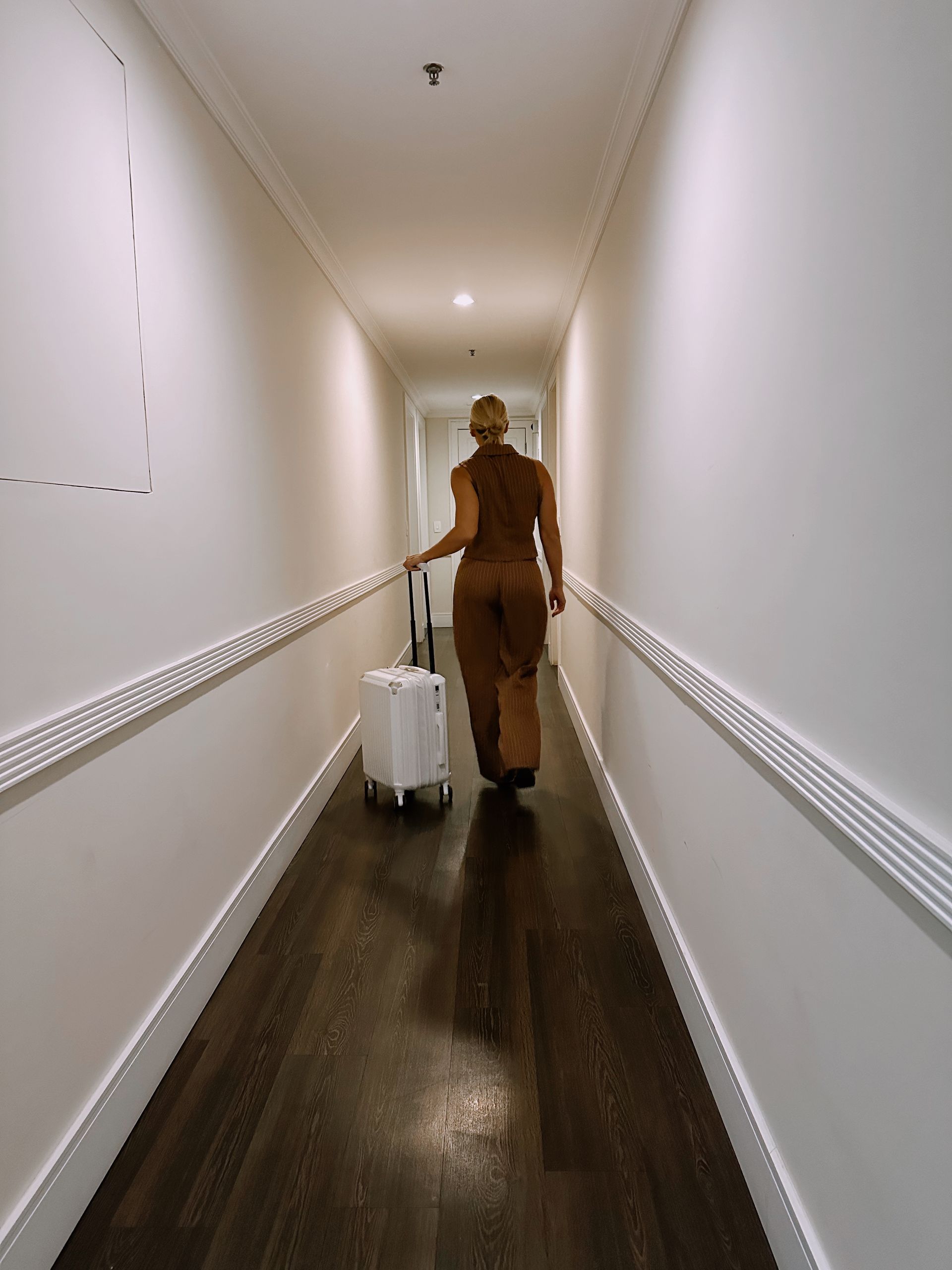 Uma mulher está caminhando por um corredor com uma mala.