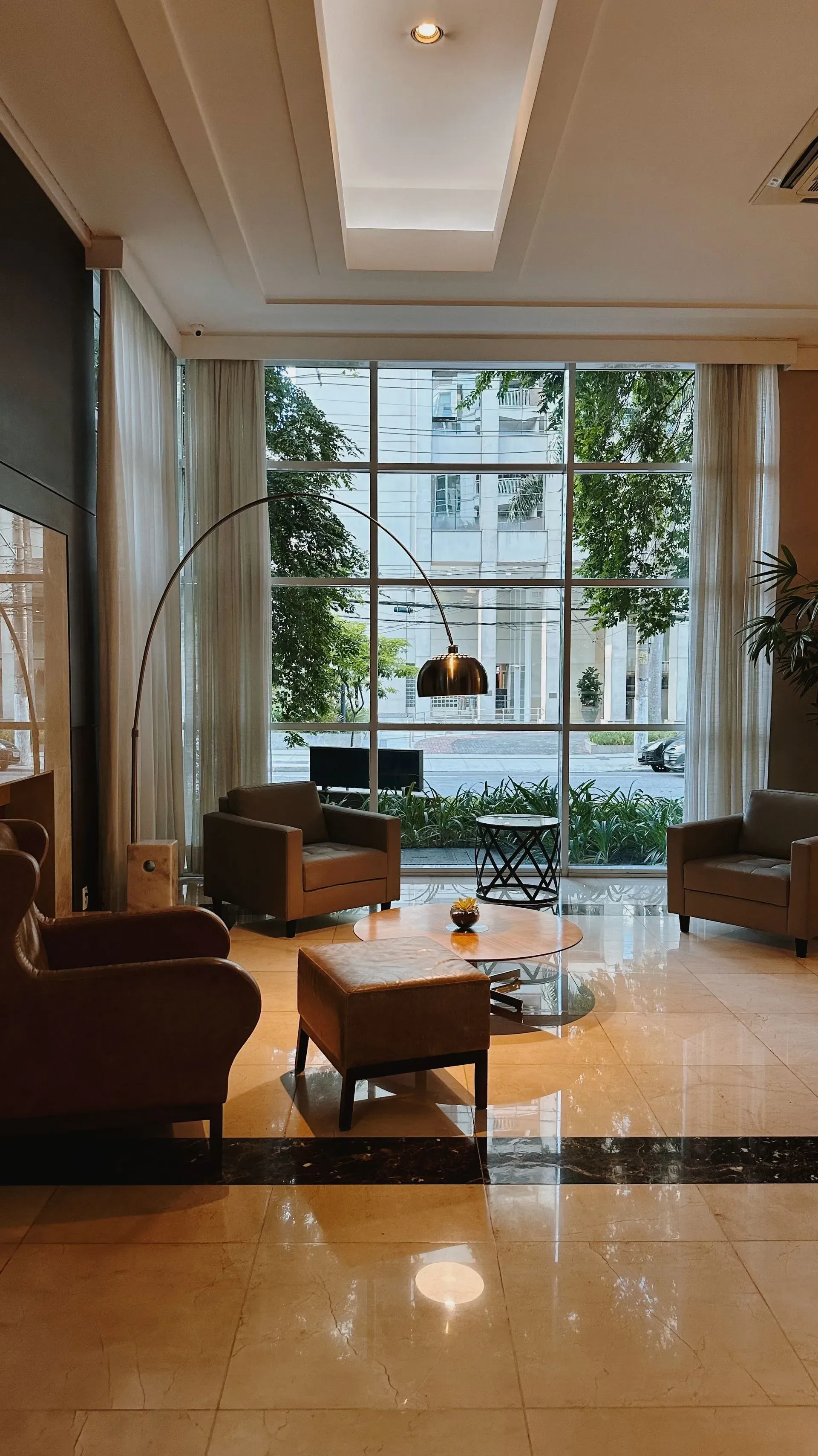 Sala de estar com mobília moderna, janelas do chão ao teto e vistas deslumbrantes do pôr do sol sobre o horizonte da cidade.