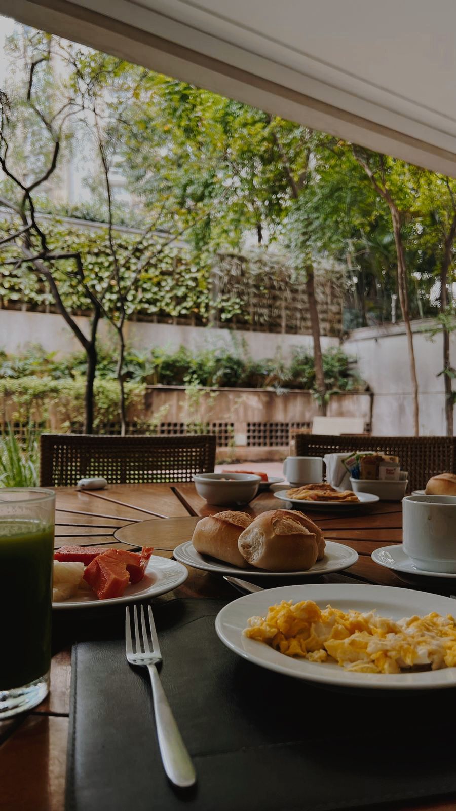 Café da manhã em área externa sofisticada do eConfor Vila Olímpia, com mesa posta e vista para um jardim arborizado de alto padrão.