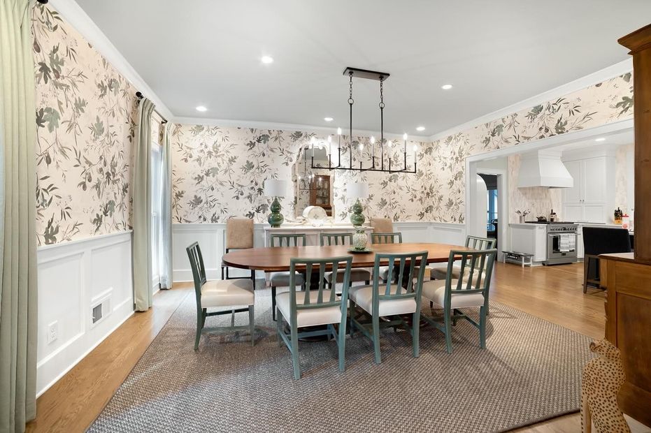 Formal dining room with floral wallpaper, oval table, chairs, and a rug.