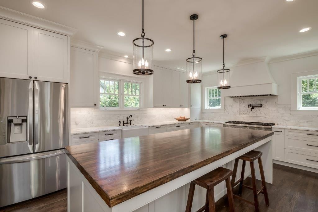 Bright kitchen with wooden island, stainless steel fridge, and white cabinets, lit by pendant lights.